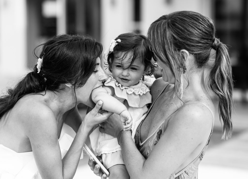 La novia y una amiga besan a una bebé en los preparativos, en blanco y negro
