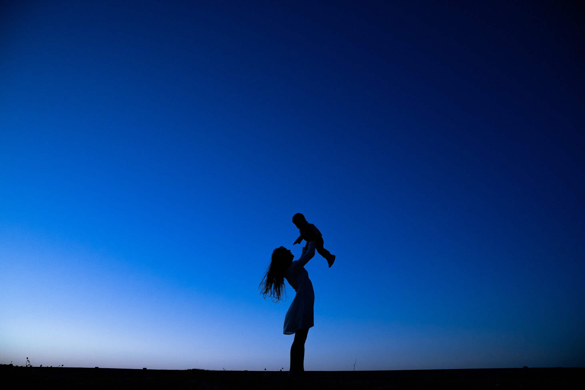 Silueta de mamá levantando a su bebé contra el cielo azul del atardecer