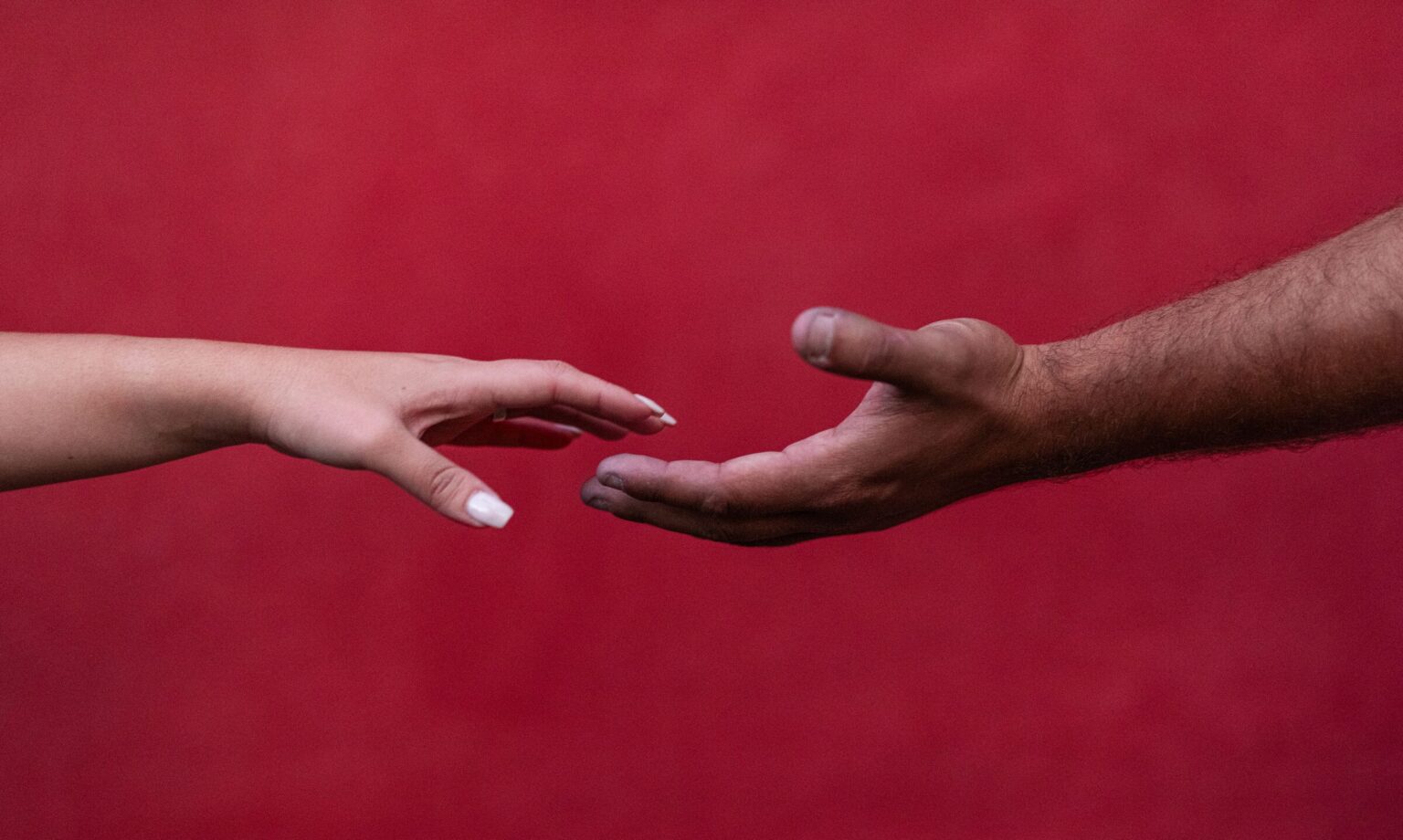 Las manos de los novios a punto de tocarse, sobre fondo rojo