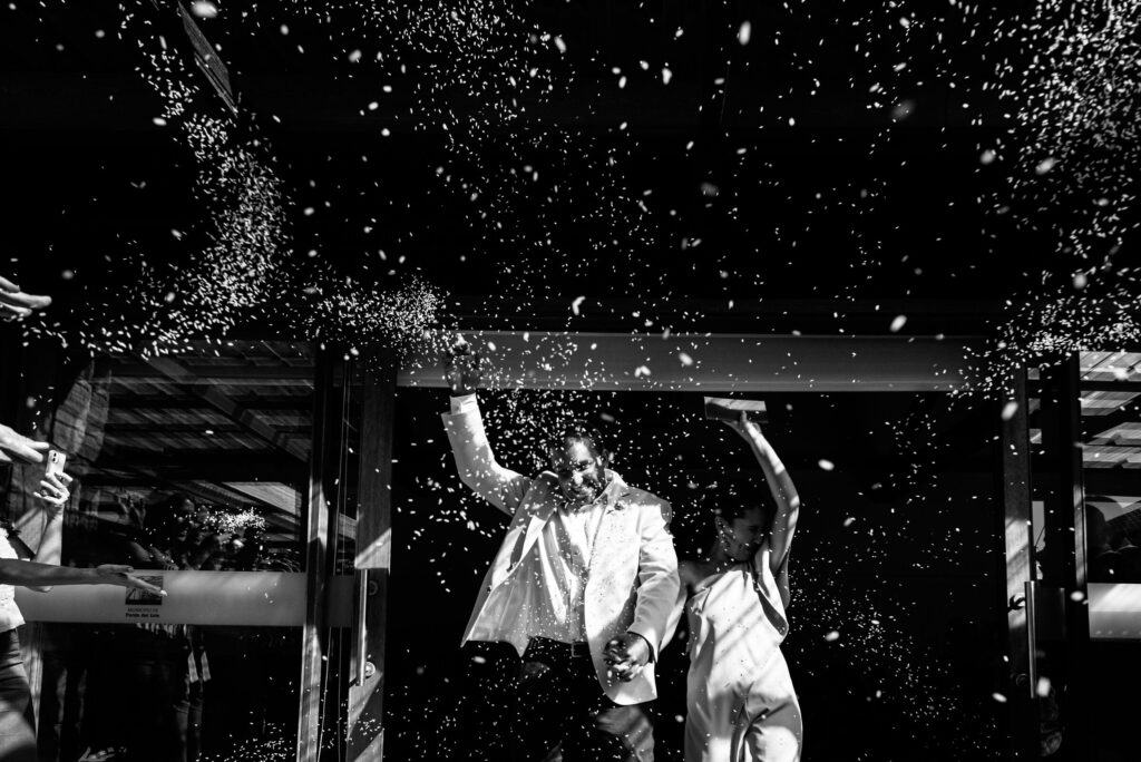 A shower of rice as the couple walks out, in black and white