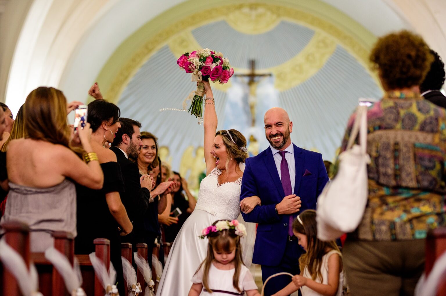 La novia levanta el ramo feliz al salir de la iglesia del brazo del novio