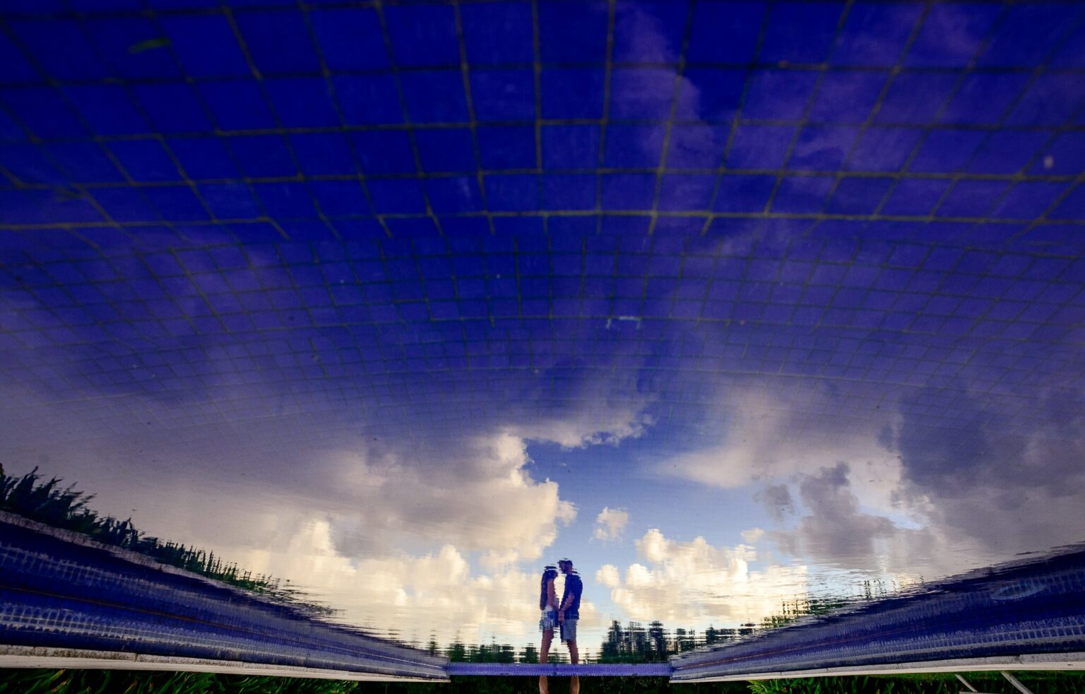 La pareja reflejada en el agua de la piscina, entre nubes