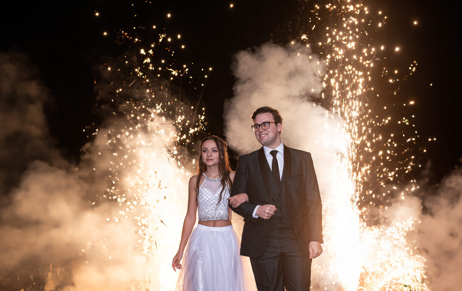 La quinceañera entra del brazo de su hermano entre fuegos artificiales y humo