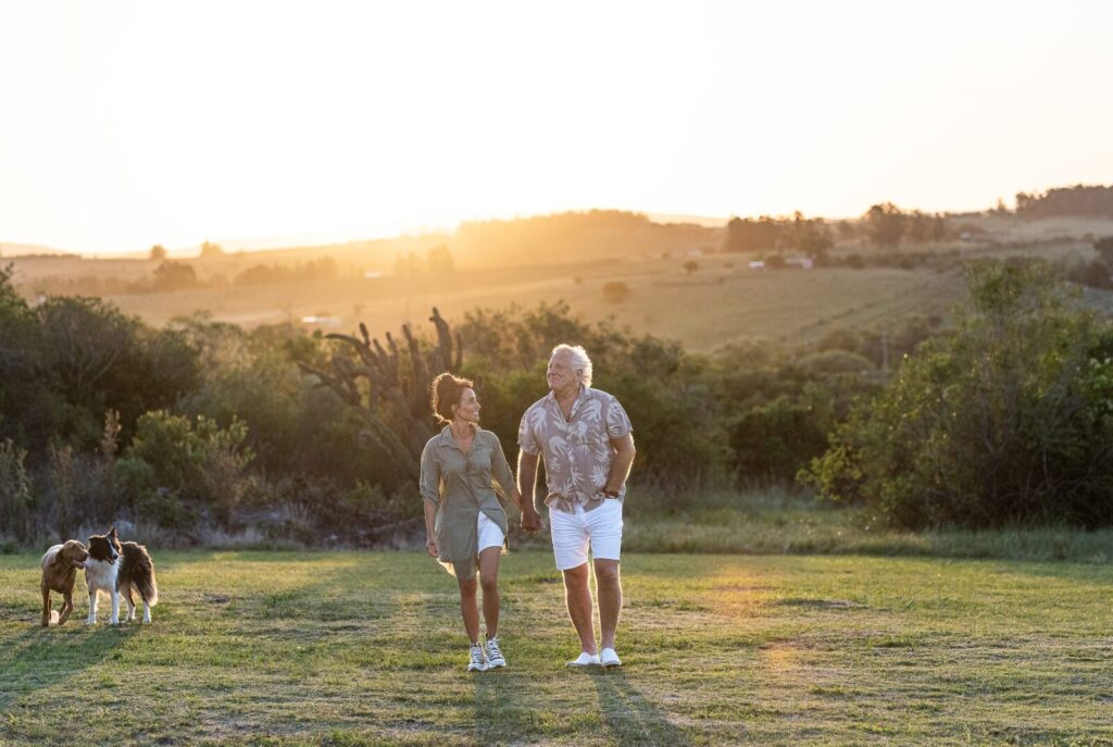 Casal caminhando com o cachorro no campo ao pôr do sol