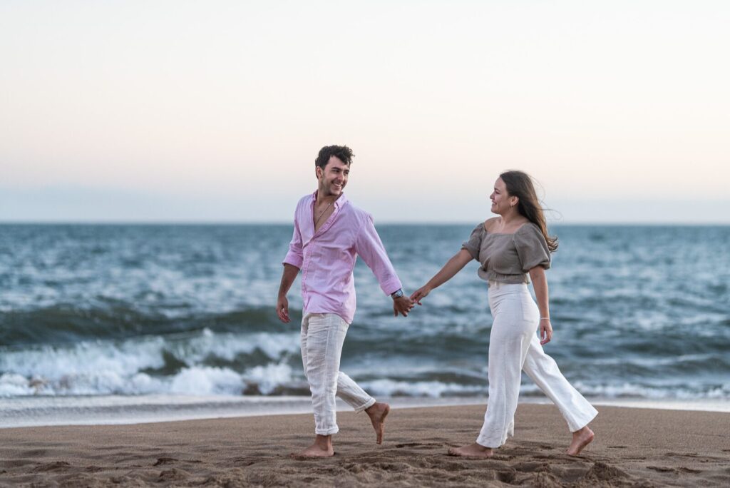 Casal caminhando de mãos dadas na beira do mar
