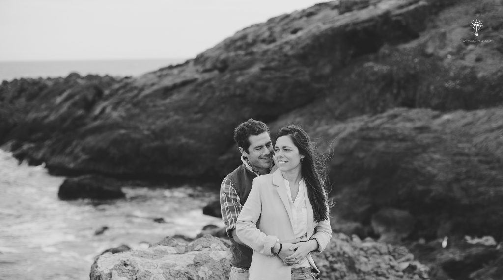 A couple embracing by the rocks and the sea, in black and white